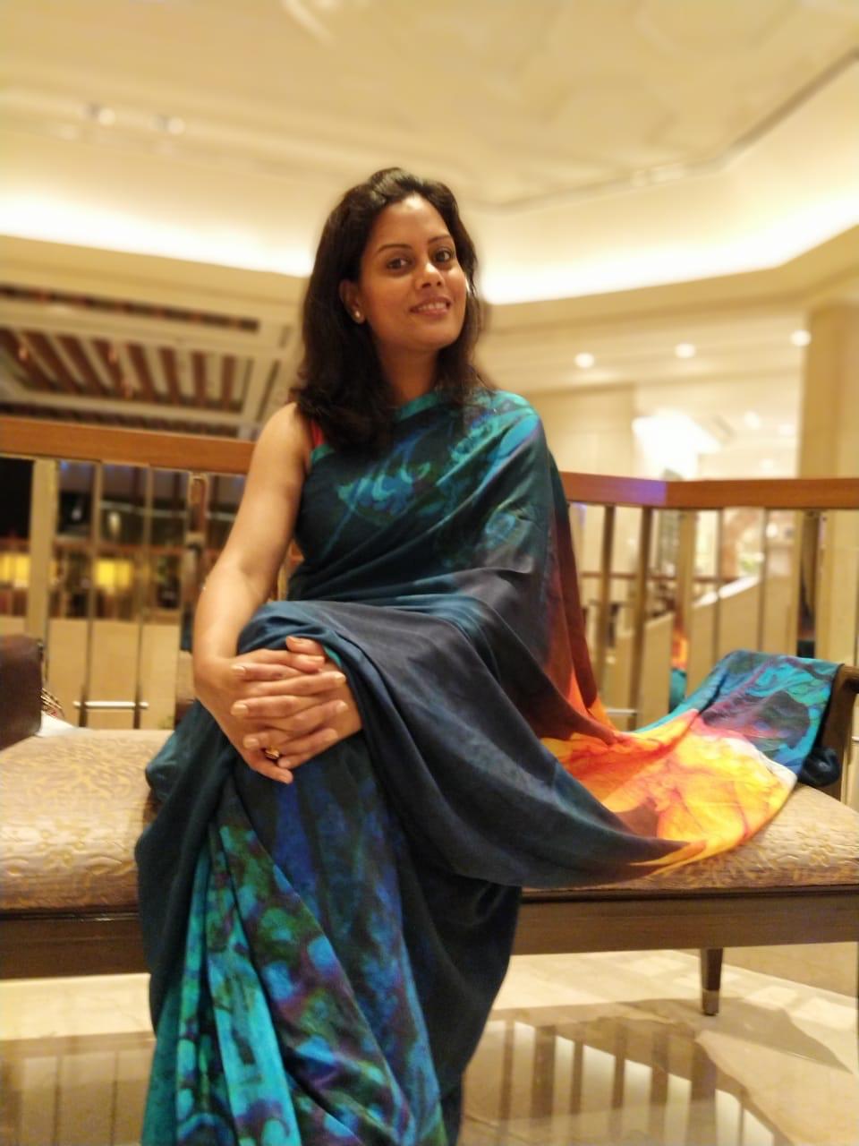 Author and writer Tanushree seated in a warmly lit setting, wearing a vibrant blue and orange Satya Paul saree